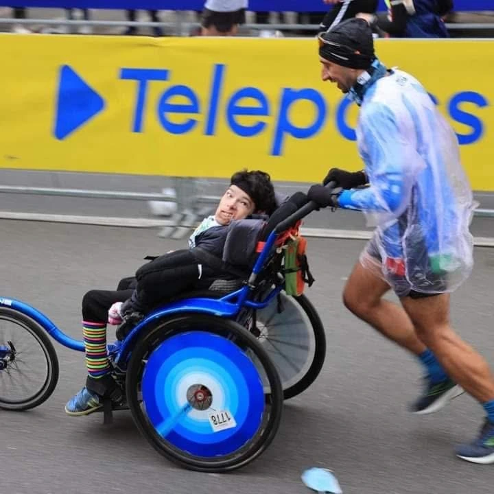 Francesco Mininni spinge carrozzina con intensità su asfalto bagnato in maratona piovosa.