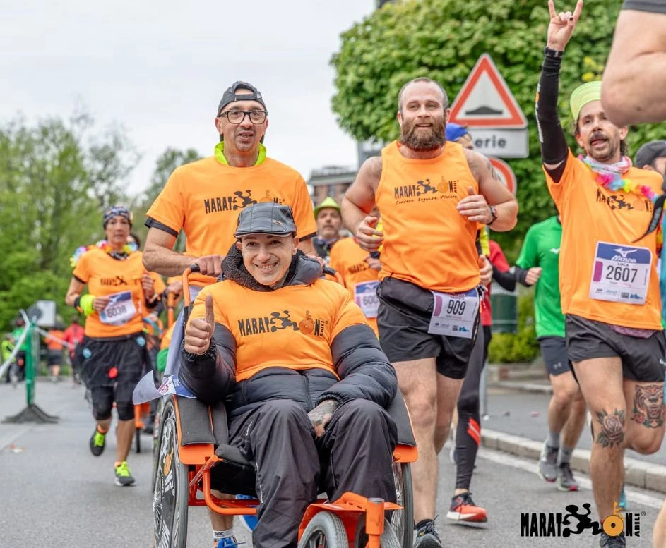 Francesco Mininni guida carrozzina nel gruppo MaratonAbili sotto arcobaleno urbano.